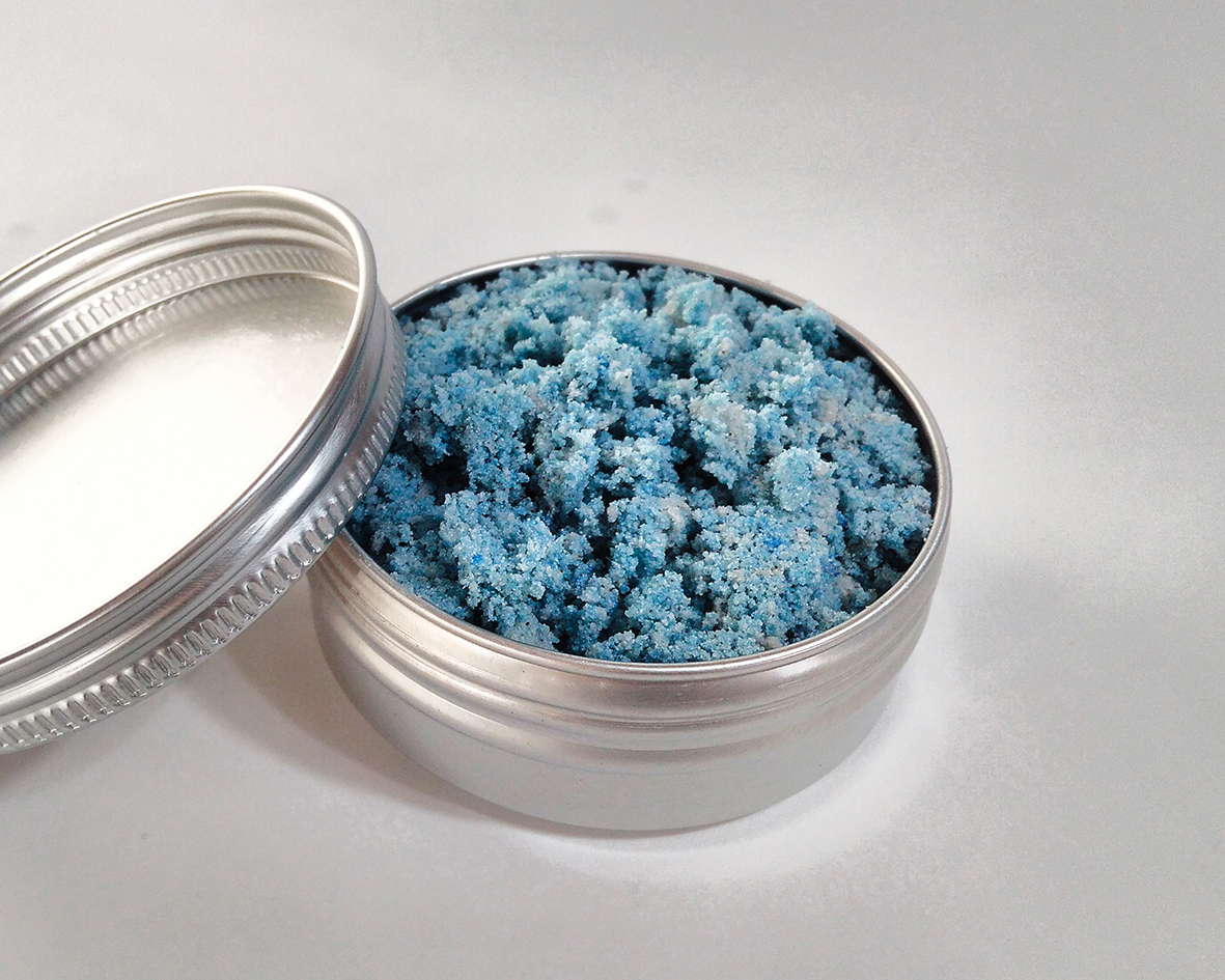 Modrý penivý sprchový peeling v hliníkovej nádobke s viečkom na bielom nekonečnom pozadí.